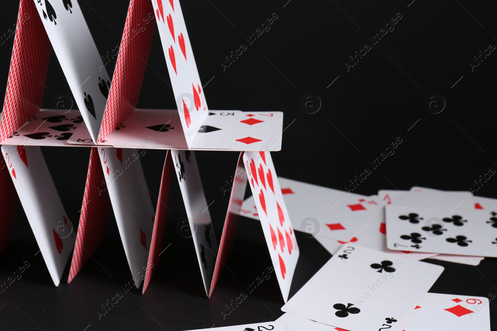 Photo of House of playing cards on black background, space for text