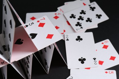 Photo of Collapsed house of playing cards on black background, closeup