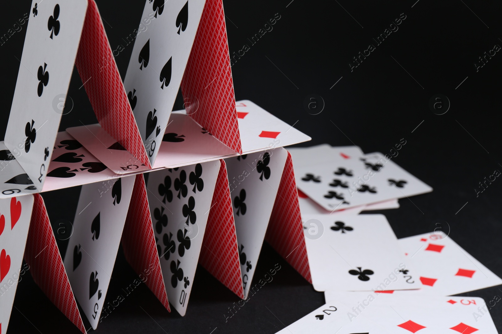 Photo of House of playing cards on black background, space for text