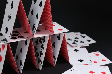 Photo of House of playing cards on black background, space for text