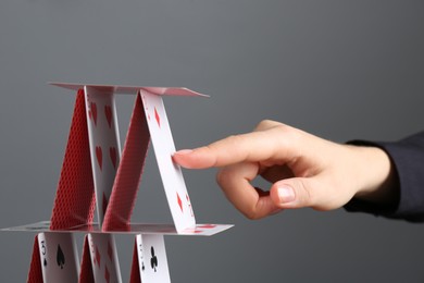 Photo of Woman destroying house of playing cards on grey background, closeup