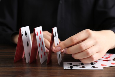 Woman building house of playing cards at wooden table, closeup