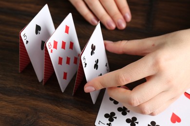 Photo of Woman building house of playing cards at wooden table, closeup