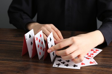 Photo of Woman building house of playing cards at wooden table, closeup