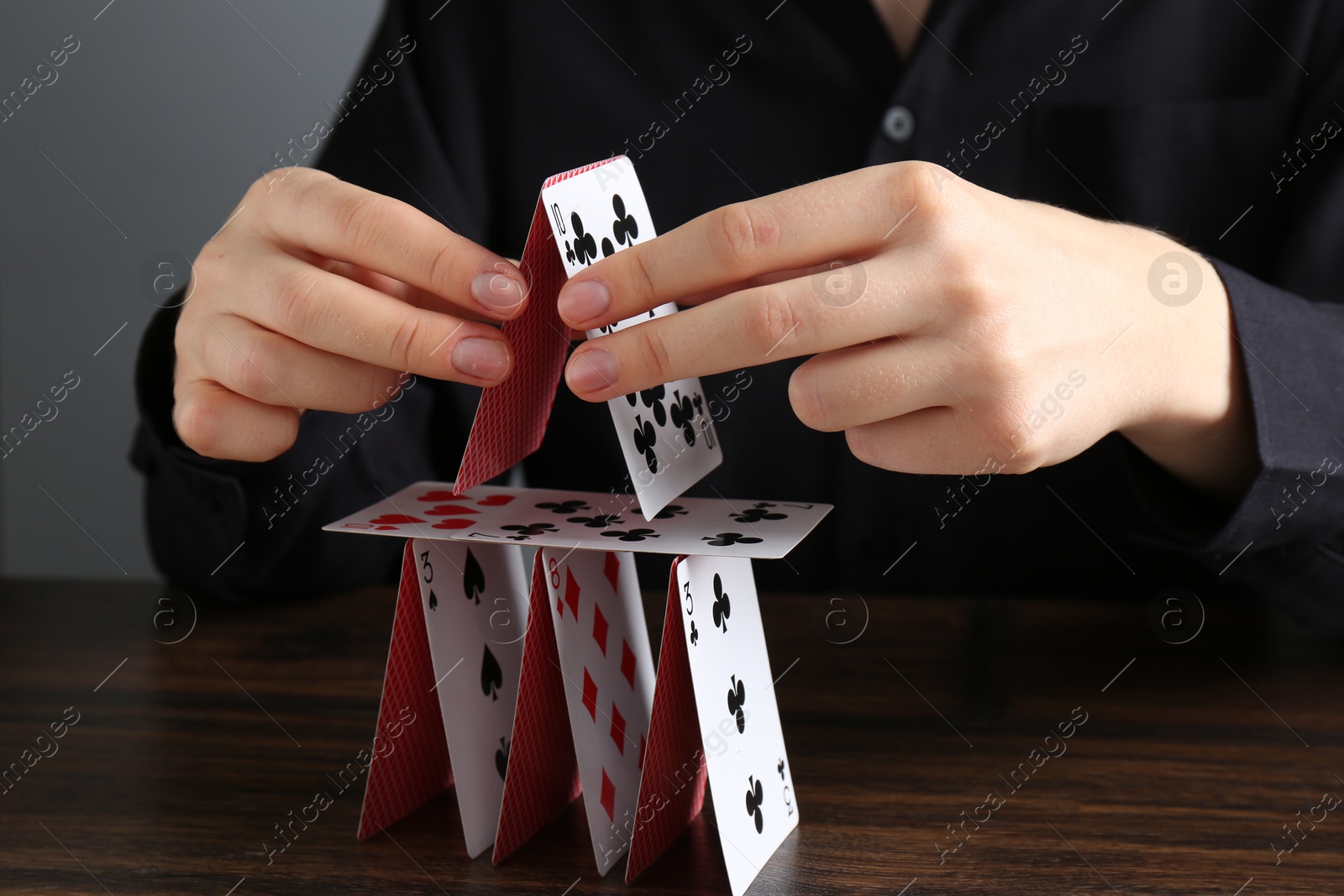 Photo of Woman building house of playing cards at wooden table, closeup