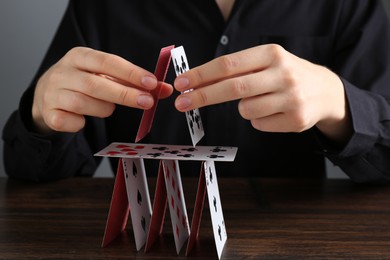 Photo of Woman building house of playing cards at wooden table, closeup