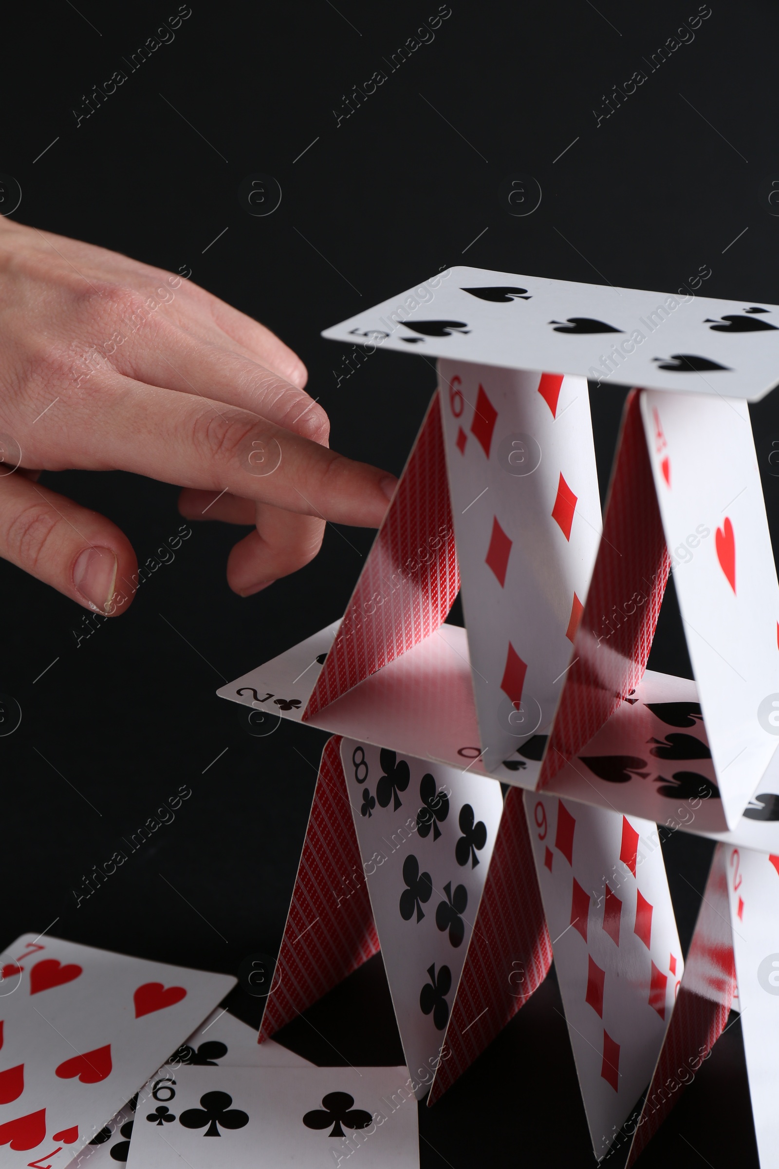 Photo of Woman destroying house of playing cards on black background, closeup