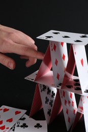 Woman destroying house of playing cards on black background, closeup