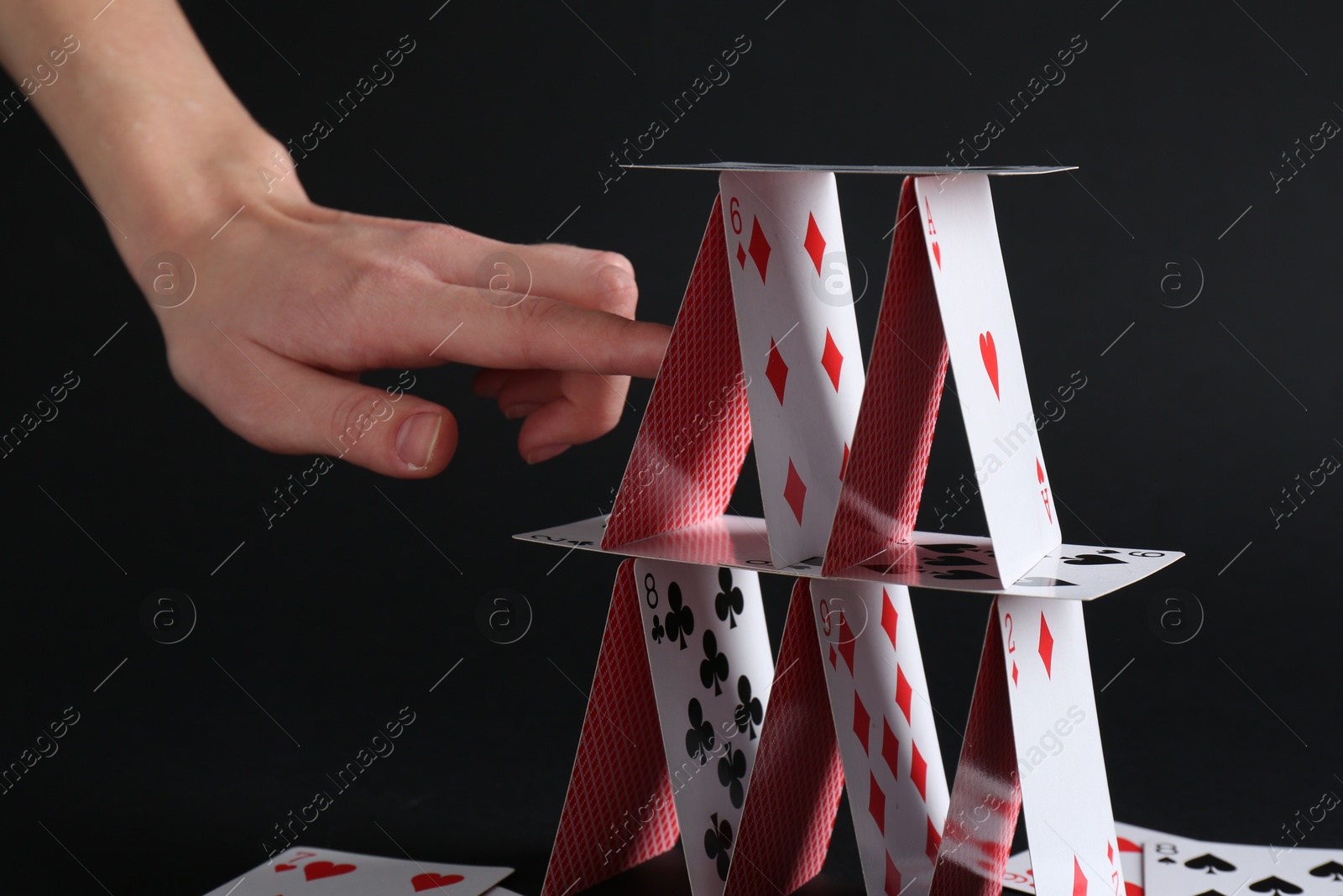 Photo of Woman destroying house of playing cards on black background, closeup