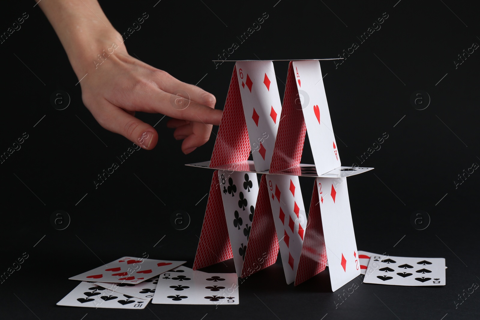 Photo of Woman destroying house of playing cards on black background, closeup