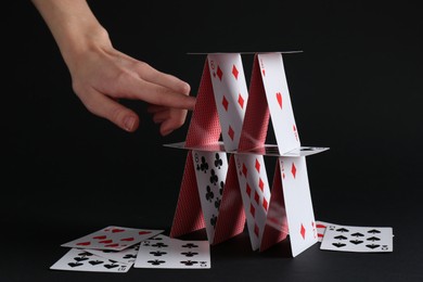 Woman destroying house of playing cards on black background, closeup