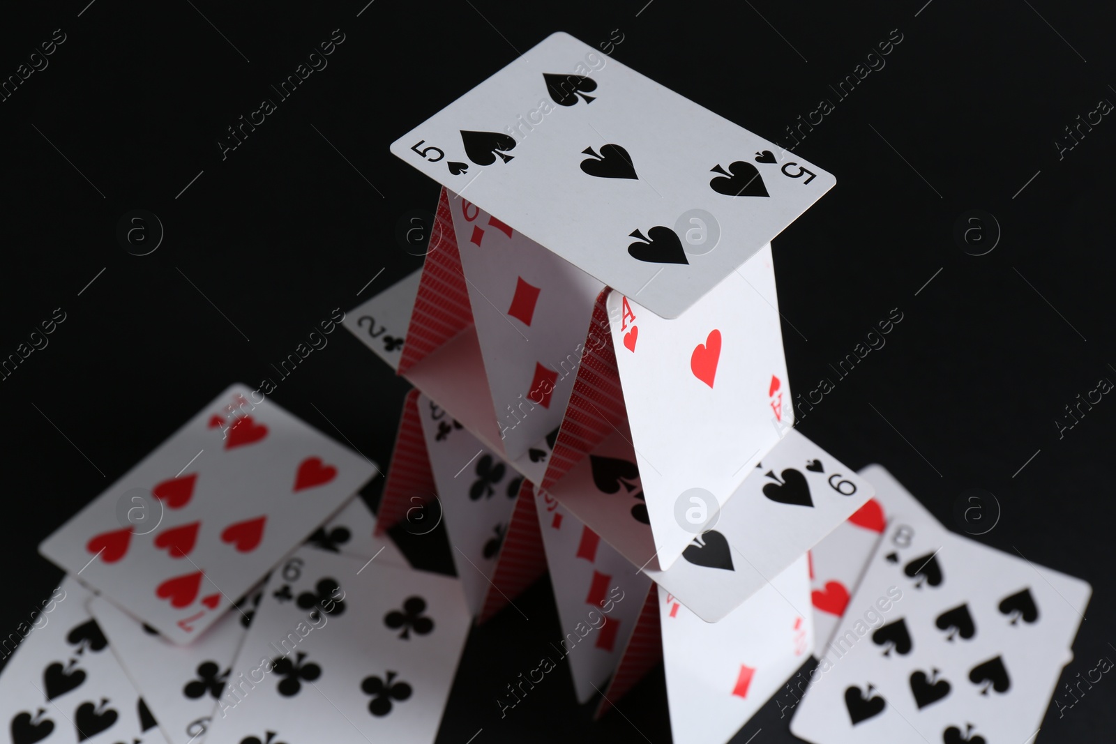 Photo of House of playing cards on black background, closeup