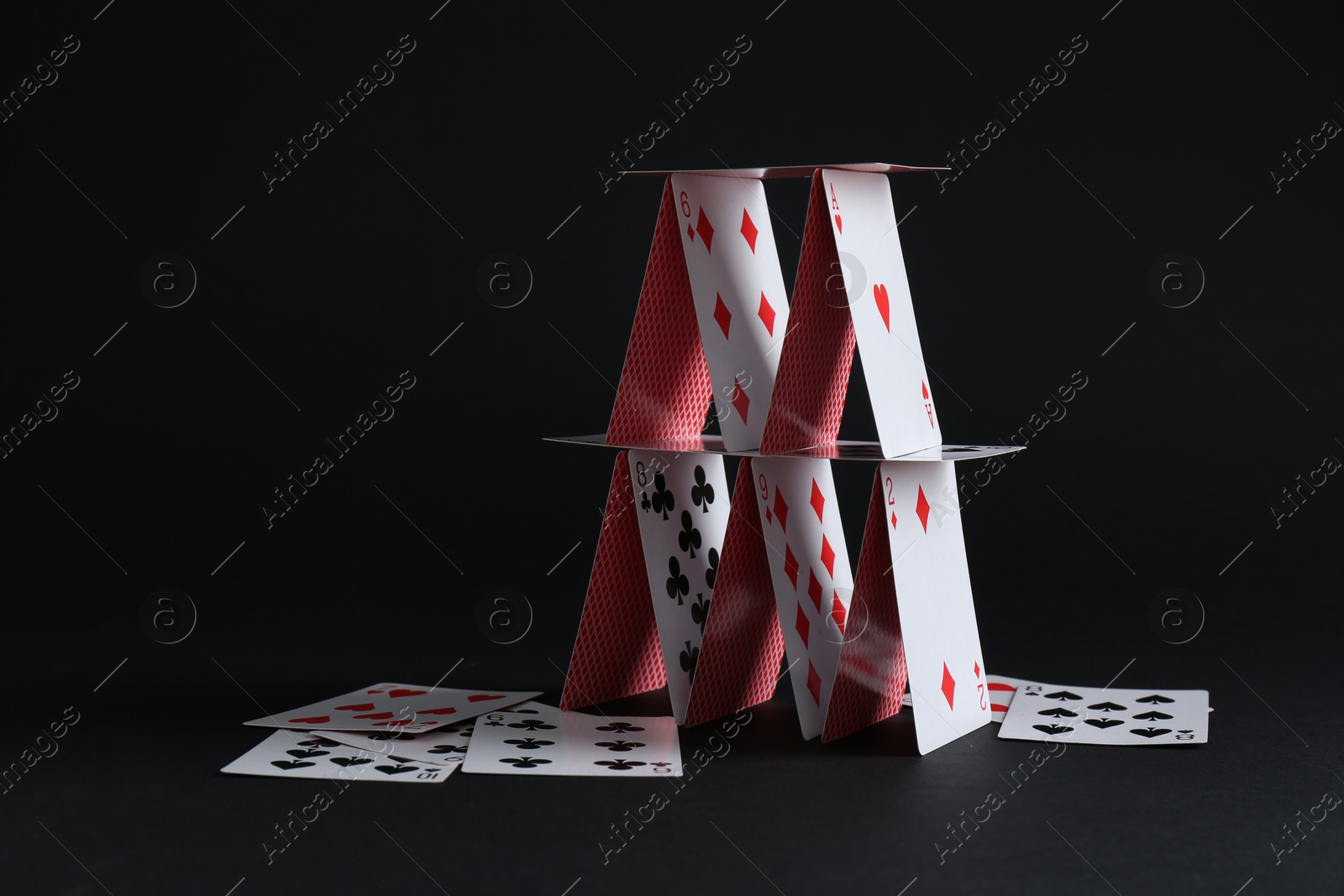 Photo of House of playing cards on black background. Space for text