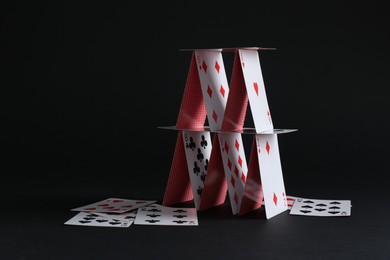 Photo of House of playing cards on black background. Space for text