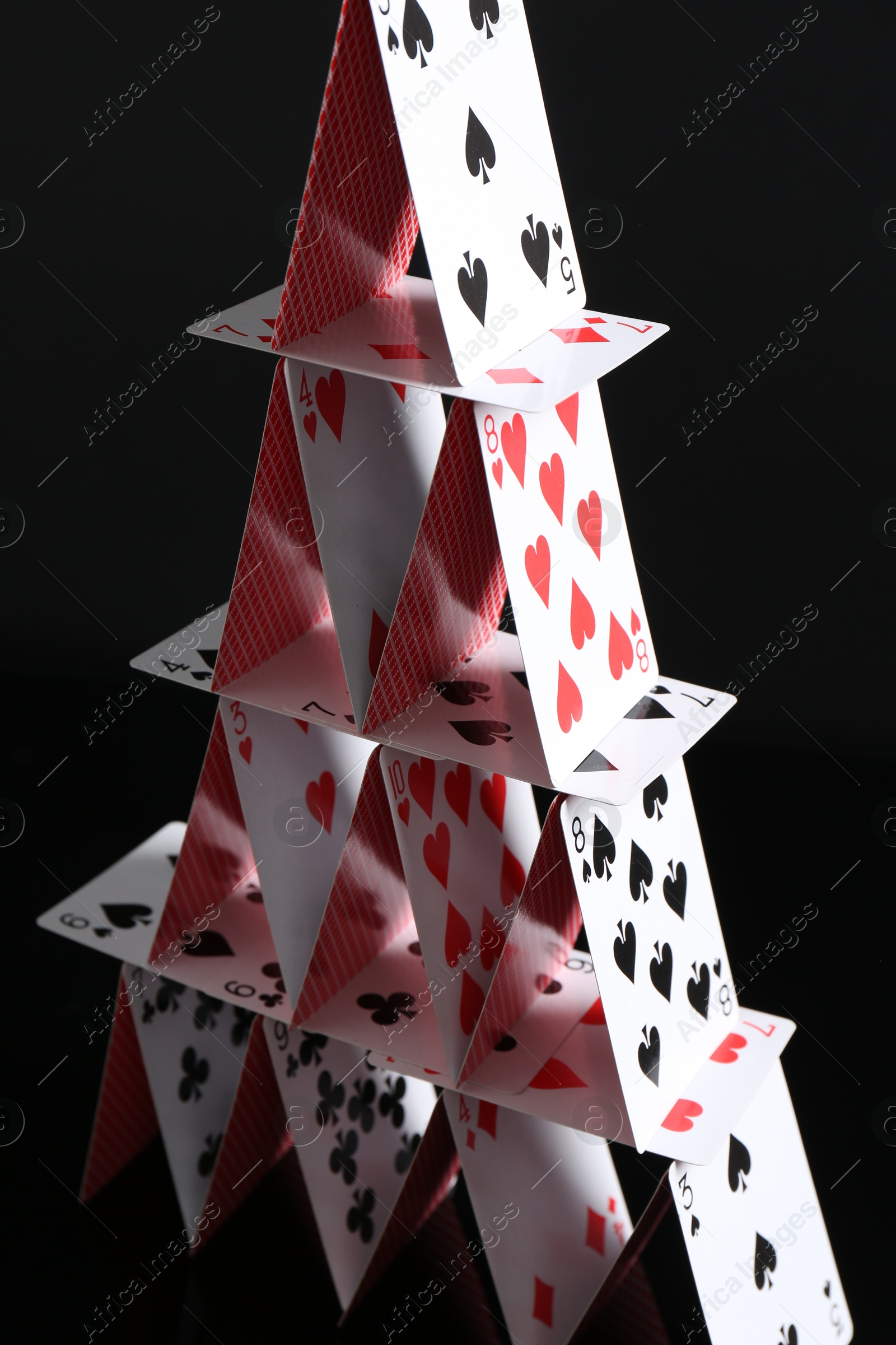 Photo of House of playing cards on black background, closeup