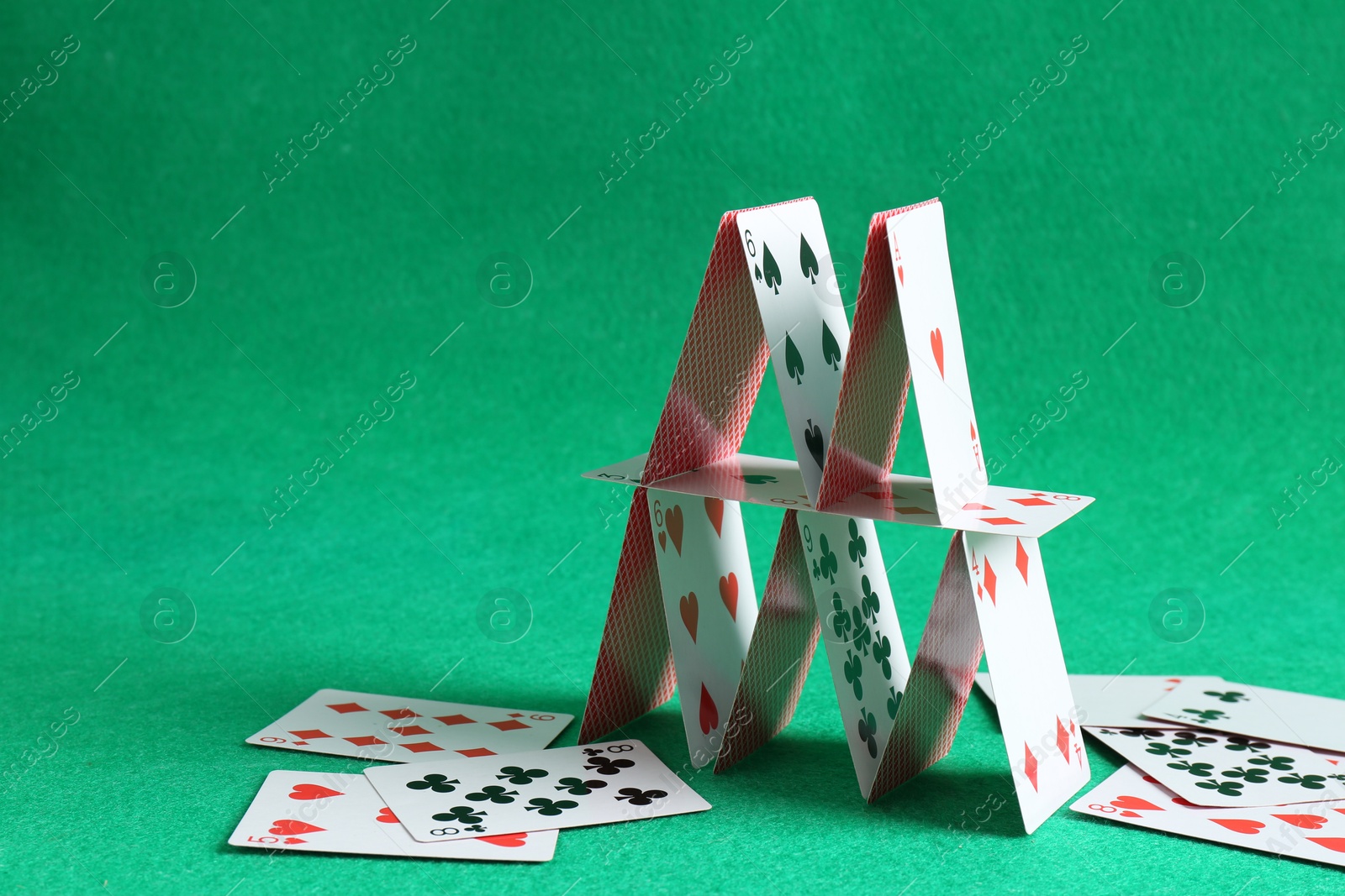 Photo of Collapsed house of playing cards on green background. Space for text