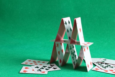 Photo of Collapsed house of playing cards on green background. Space for text