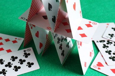 Photo of House of playing cards on green background, closeup