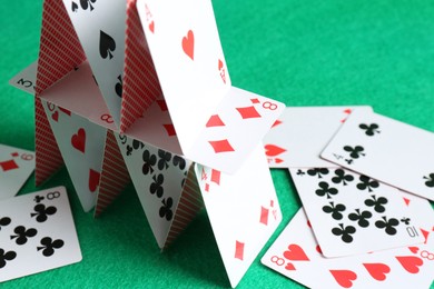 Photo of House of playing cards on green background, closeup