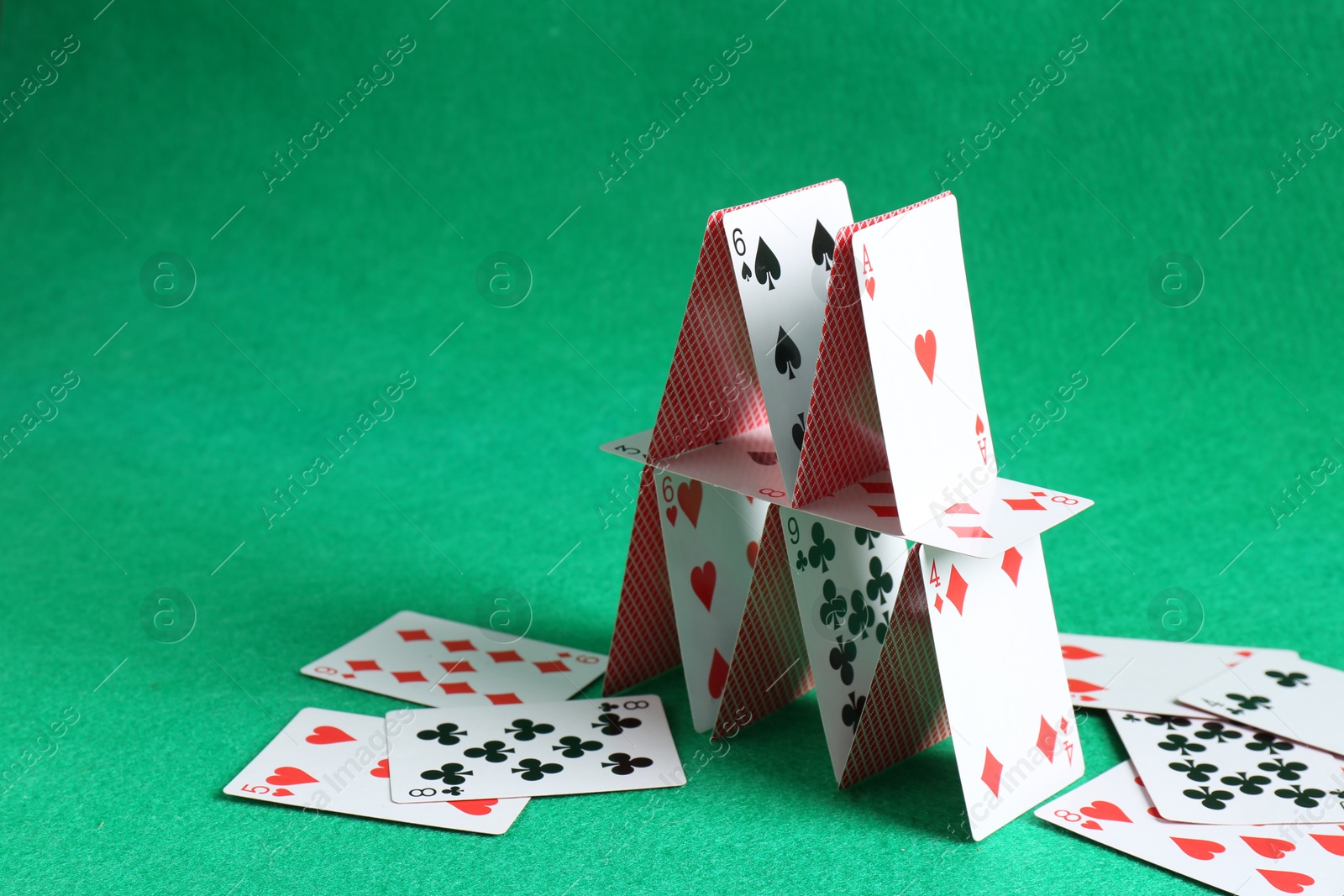 Photo of Collapsed house of playing cards on green background. Space for text