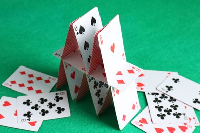 Photo of Collapsed house of playing cards on green background, closeup