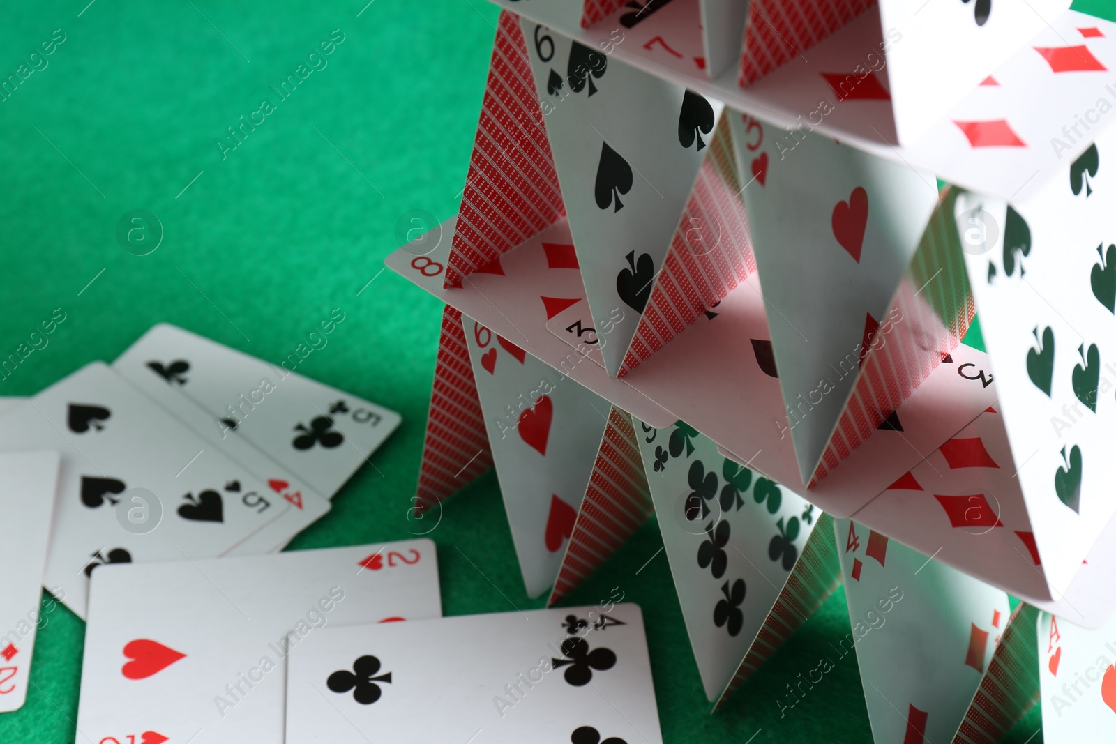 Photo of House of playing cards on green background, closeup