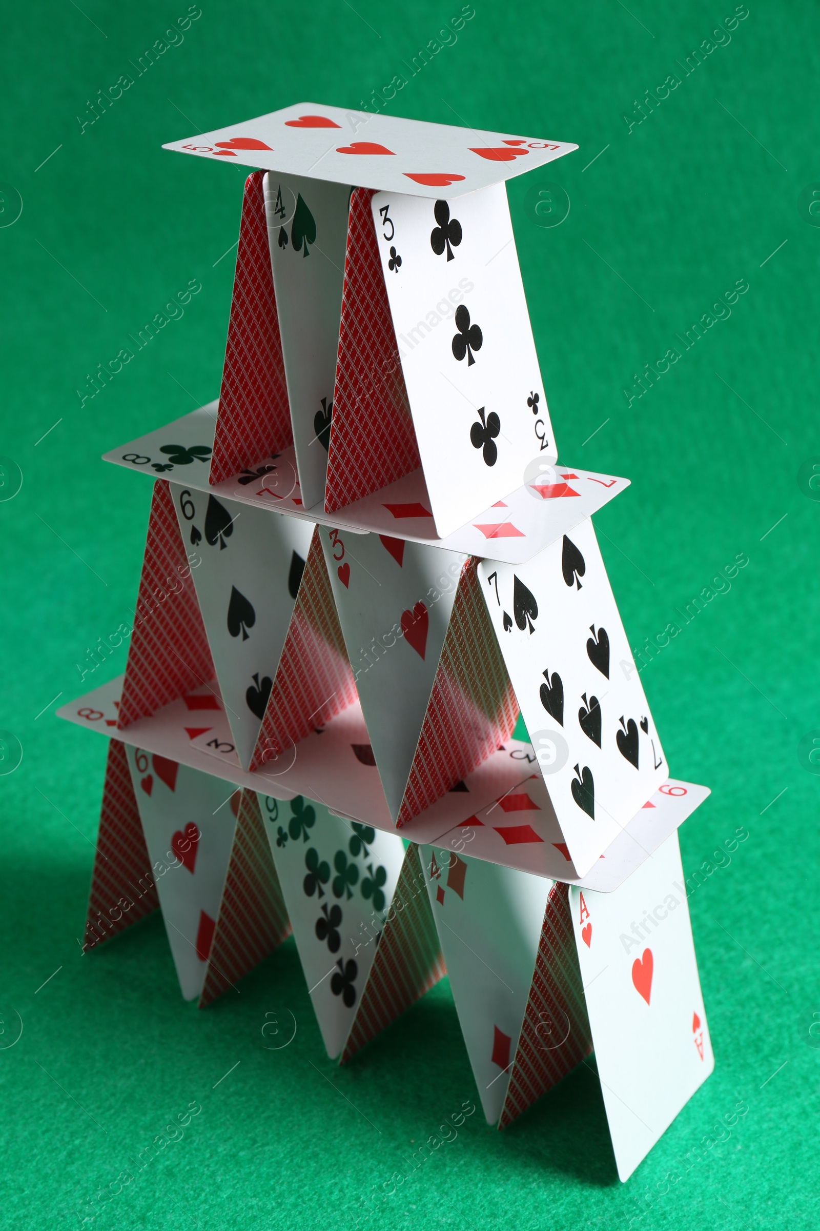 Photo of House of playing cards on green background, closeup