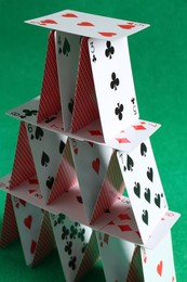 Photo of House of playing cards on green background, closeup