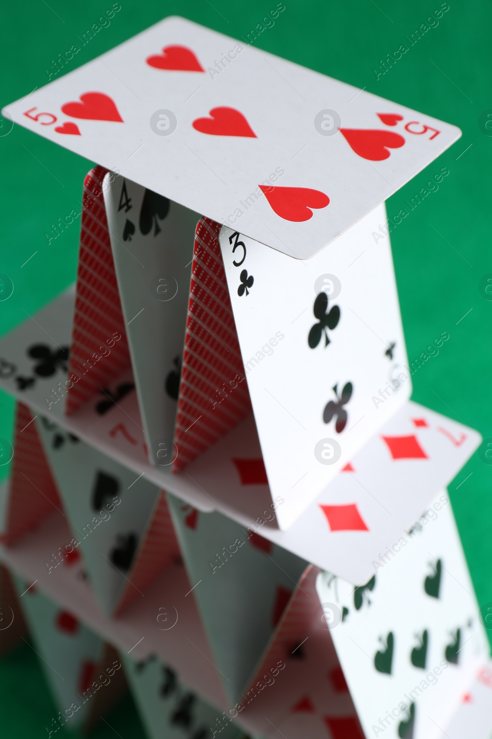 Photo of House of playing cards on green background, closeup