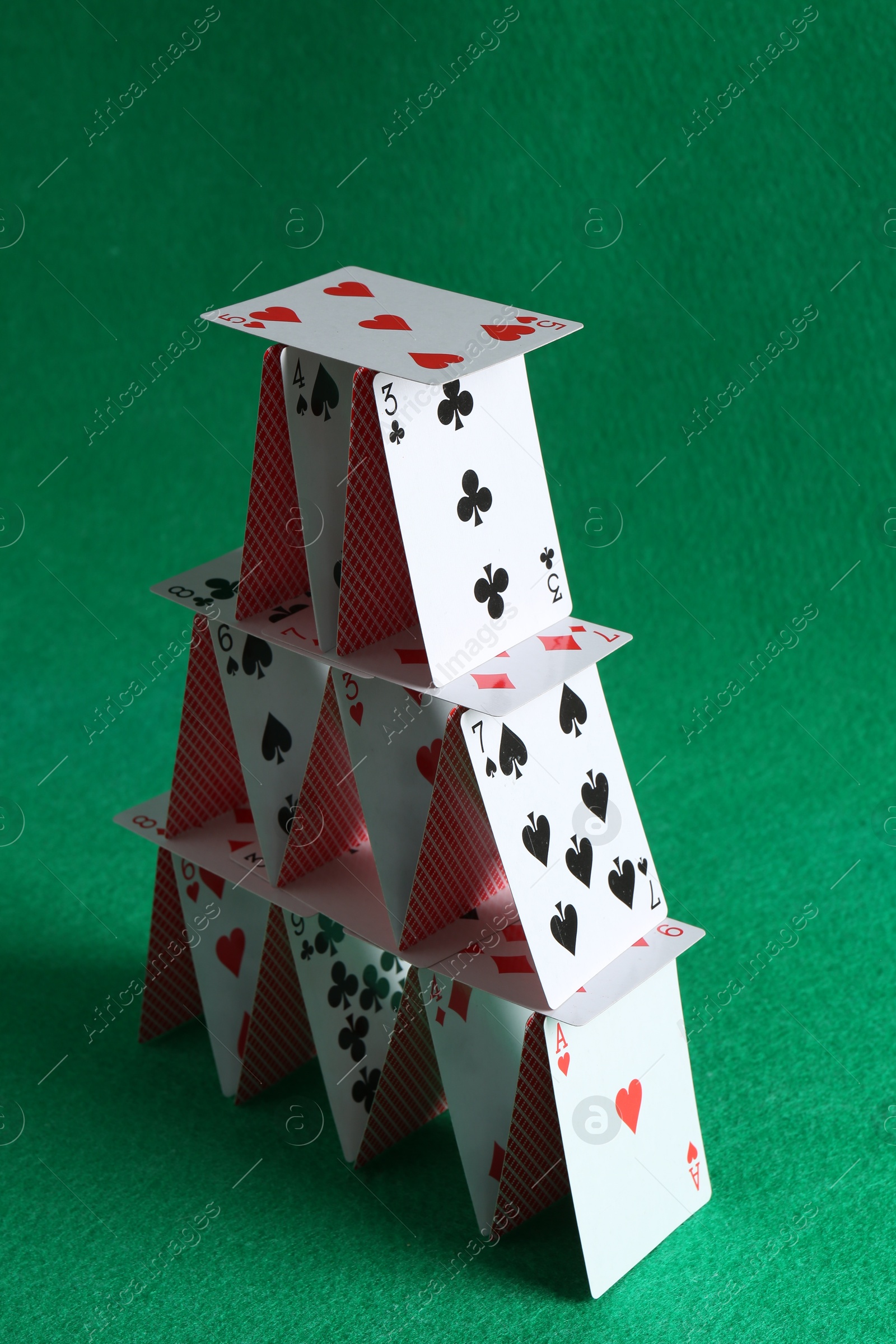 Photo of House of playing cards on green background