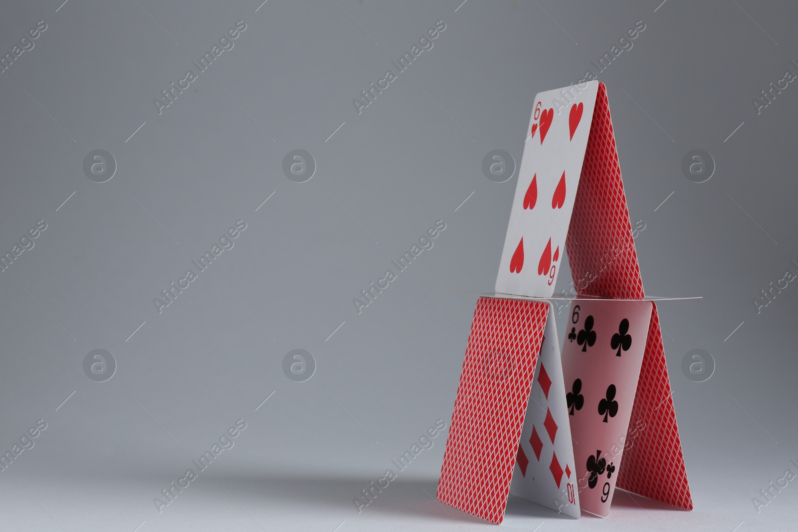 Photo of House of playing cards on light grey background. Space for text