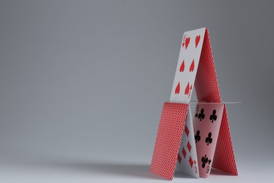 Photo of House of playing cards on light grey background. Space for text