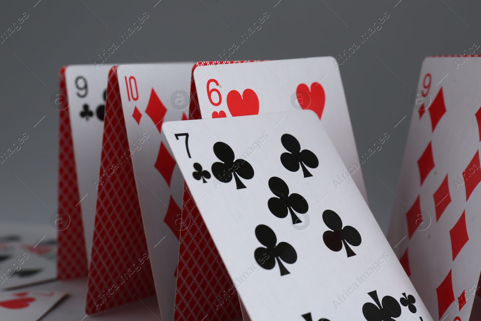 Photo of Collapsed house of playing cards on grey background, closeup