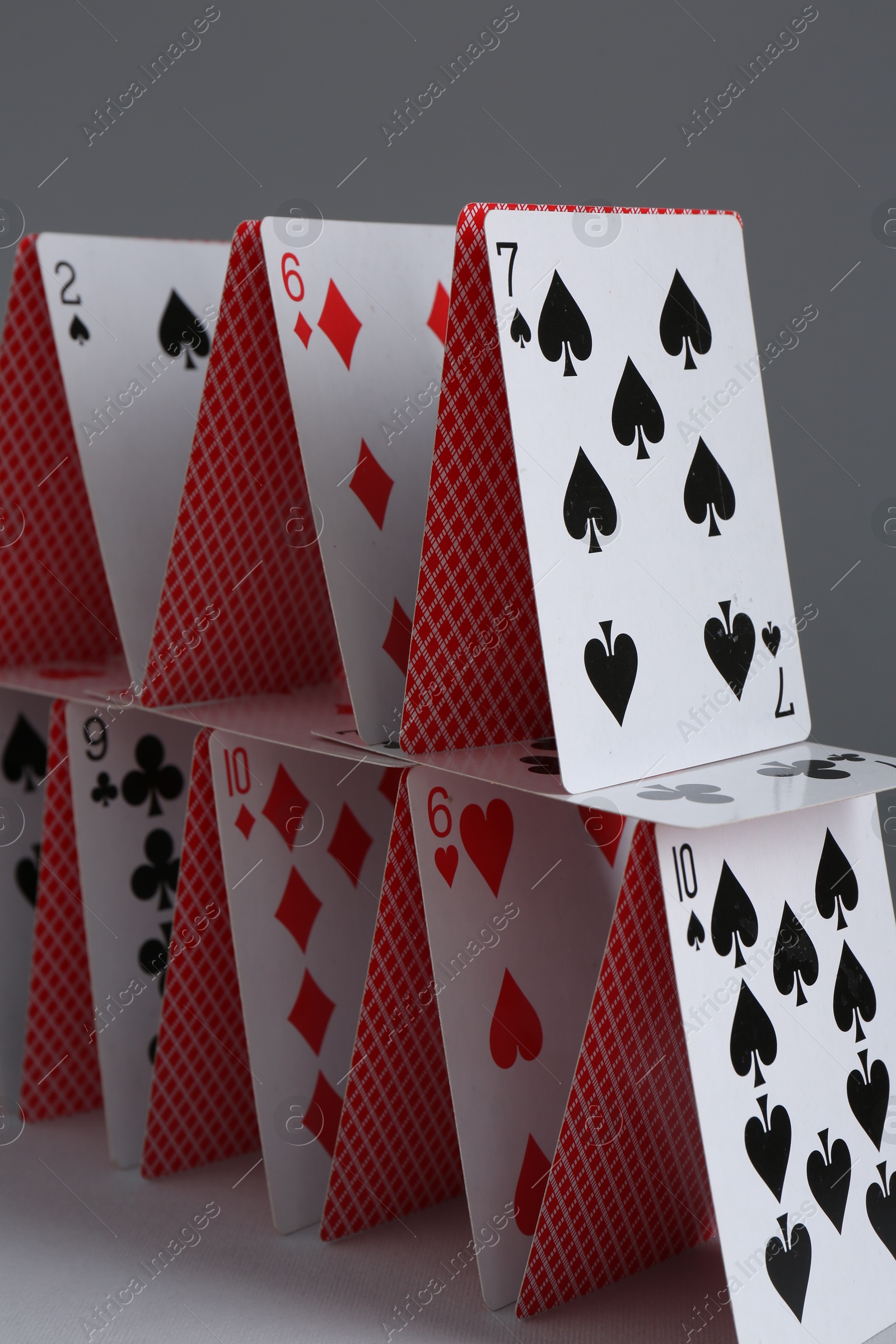 Photo of House of playing cards on grey background, closeup