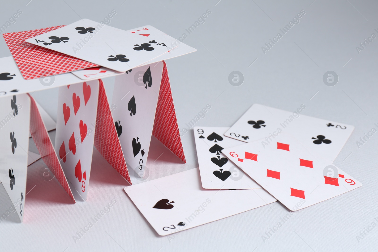 Photo of Collapsed house of playing cards on light grey background, closeup