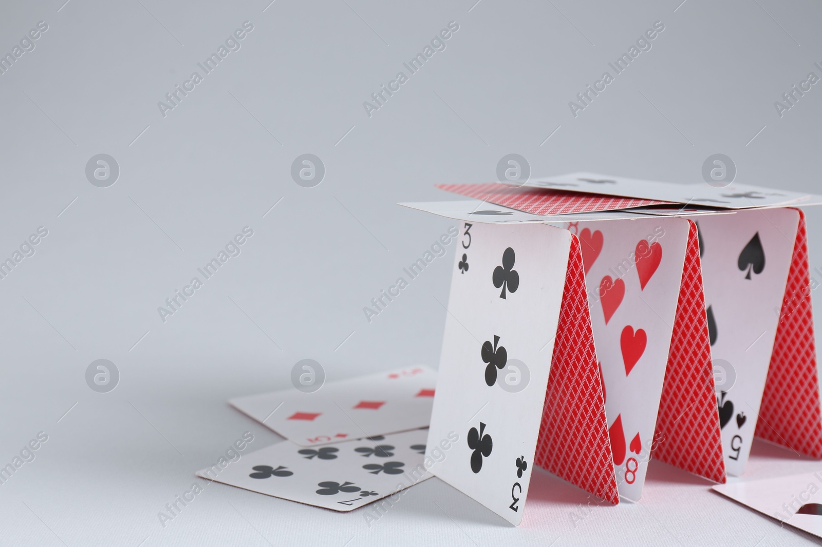 Photo of Collapsed house of playing cards on light grey background, closeup. Space for text