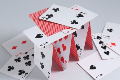 Photo of Collapsed house of playing cards on light grey background, closeup