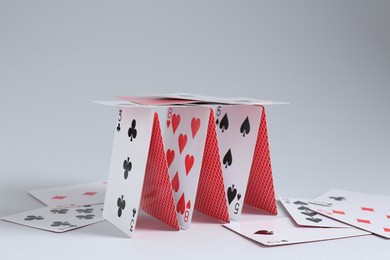 Photo of Collapsed house of playing cards on light grey background, closeup