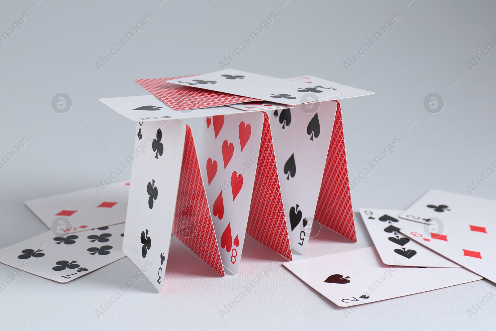 Photo of Collapsed house of playing cards on light grey background, closeup