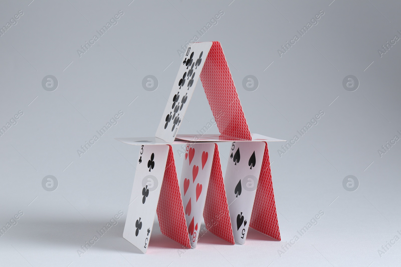 Photo of House of playing cards on light grey background