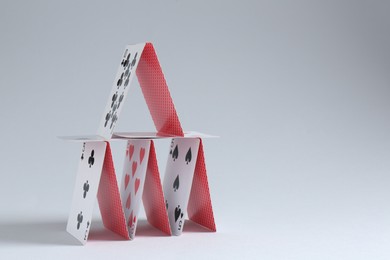 Photo of House of playing cards on light grey background. Space for text