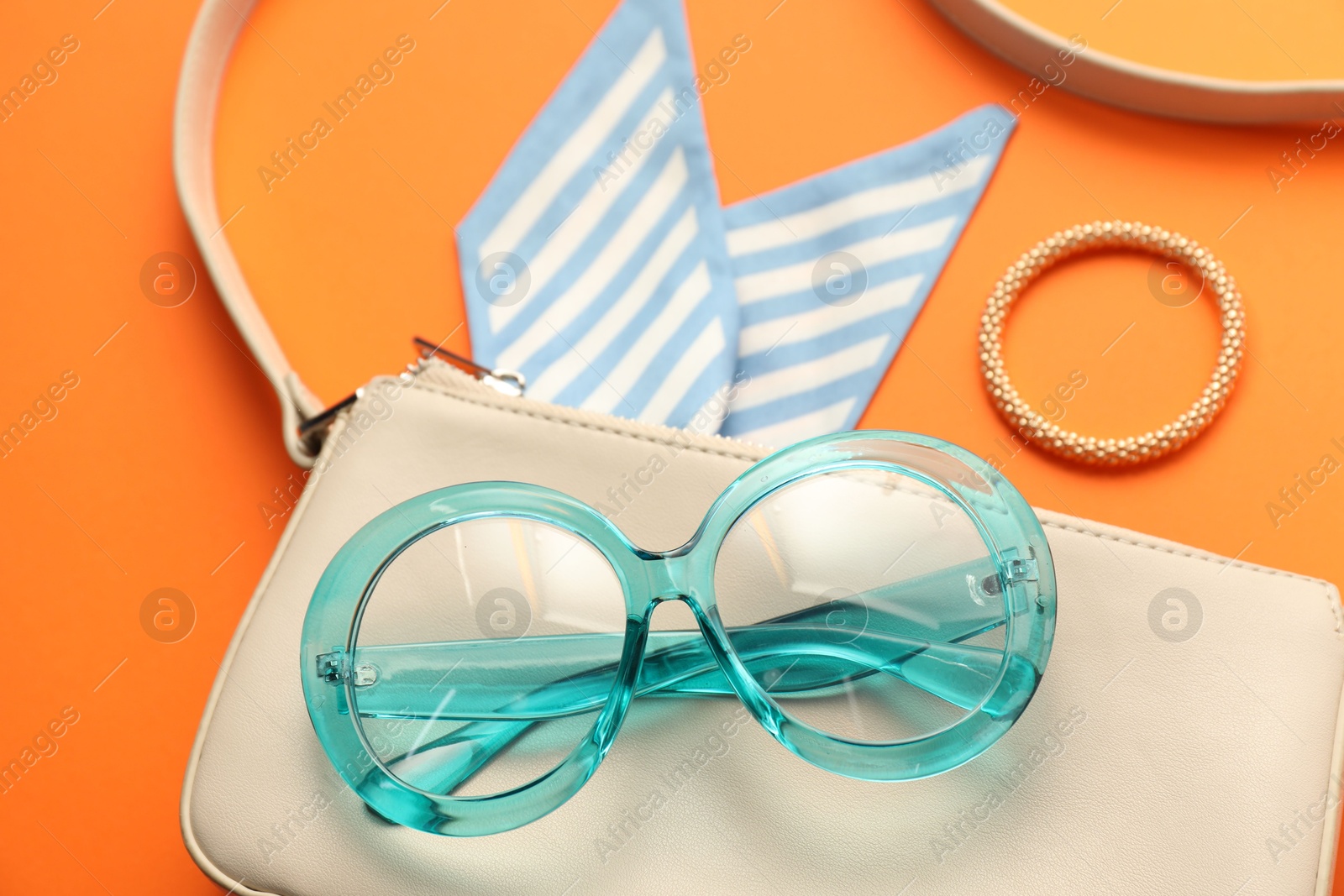 Photo of Stylish light blue glasses and other accessories on orange background, closeup