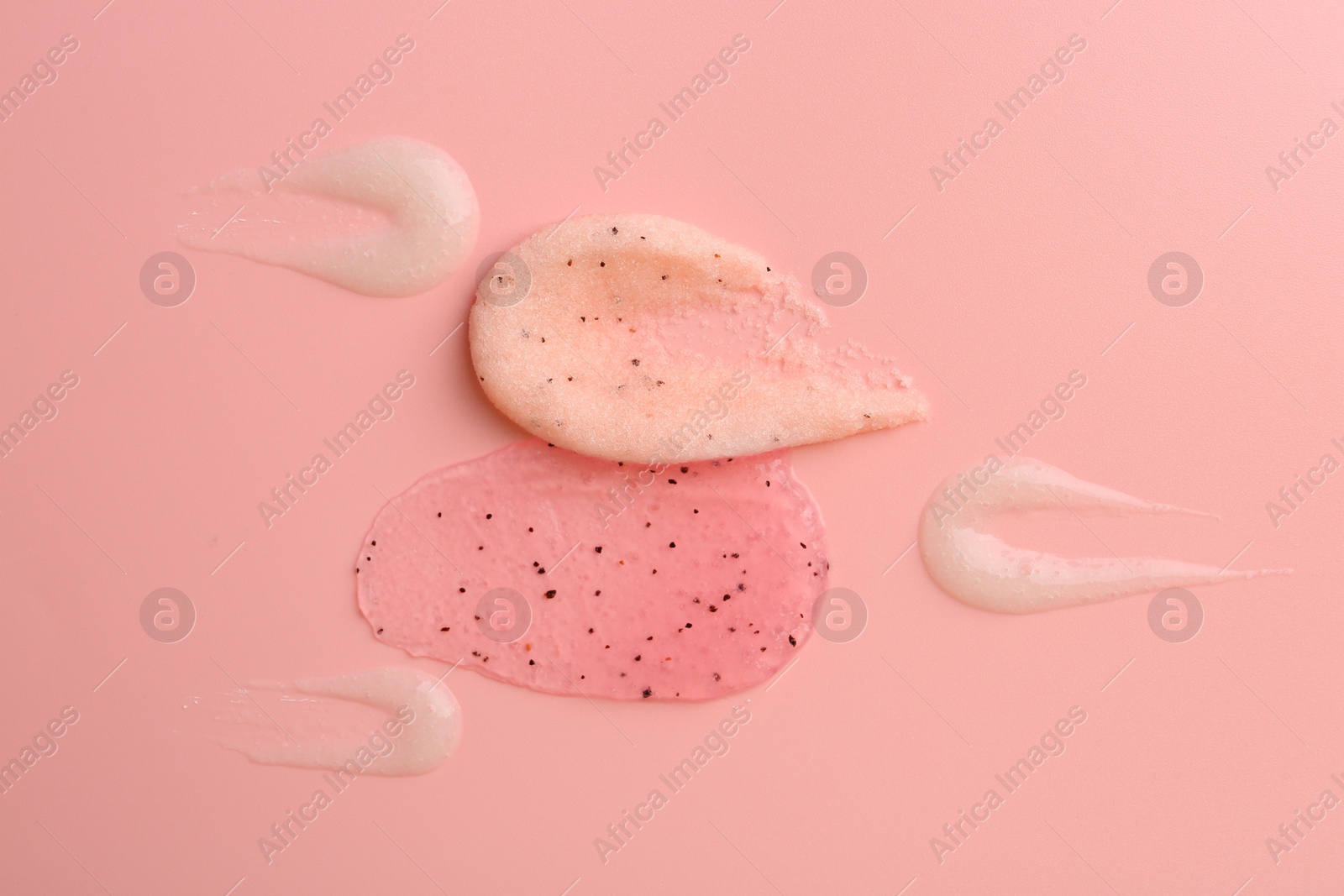 Photo of Smears of body scrubs on light pink background, flat lay