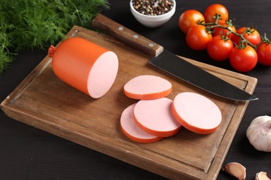 Photo of Tasty boiled sausage, knife, spices and tomatoes on black wooden table