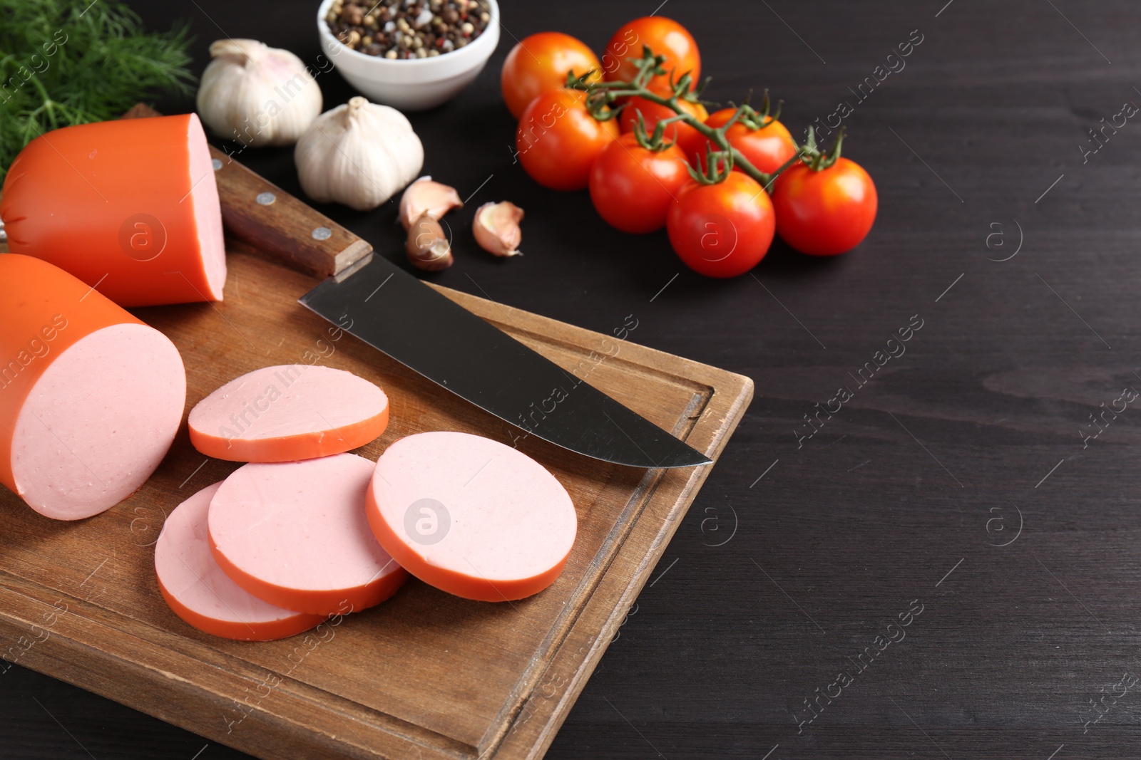 Photo of Tasty boiled sausage, knife, spices and tomatoes on black wooden table, space for text