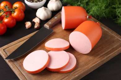 Photo of Tasty boiled sausage, knife, spices and tomatoes on black wooden table, closeup