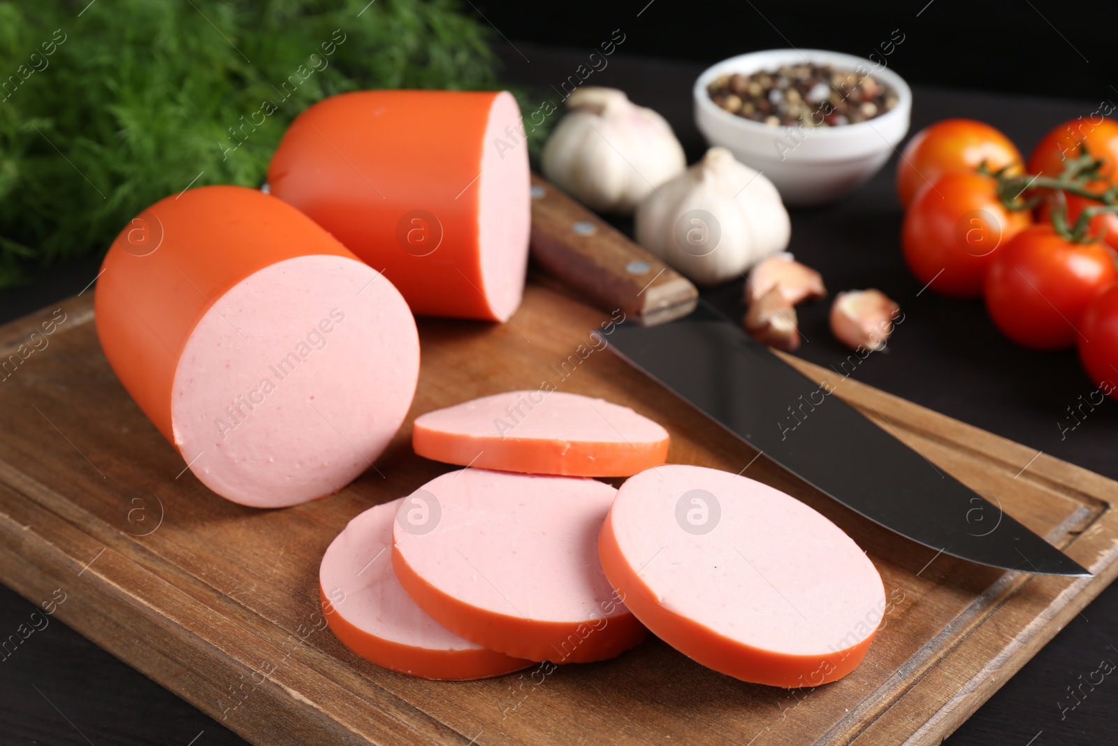 Photo of Tasty boiled sausage, knife, spices and tomatoes on table, closeup