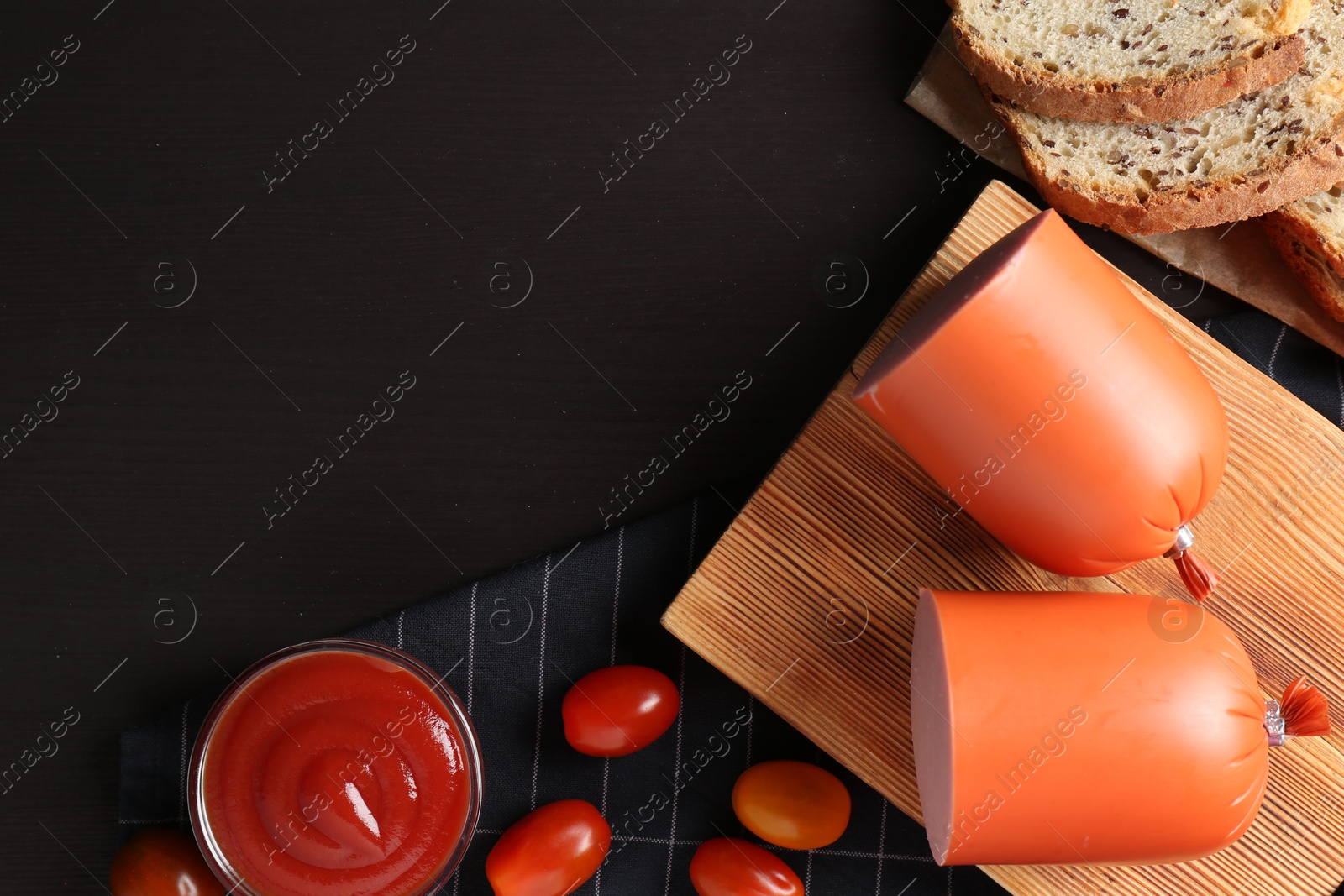 Photo of Tasty boiled sausage, ketchup, tomatoes and bread on black wooden table, top view. Space for text