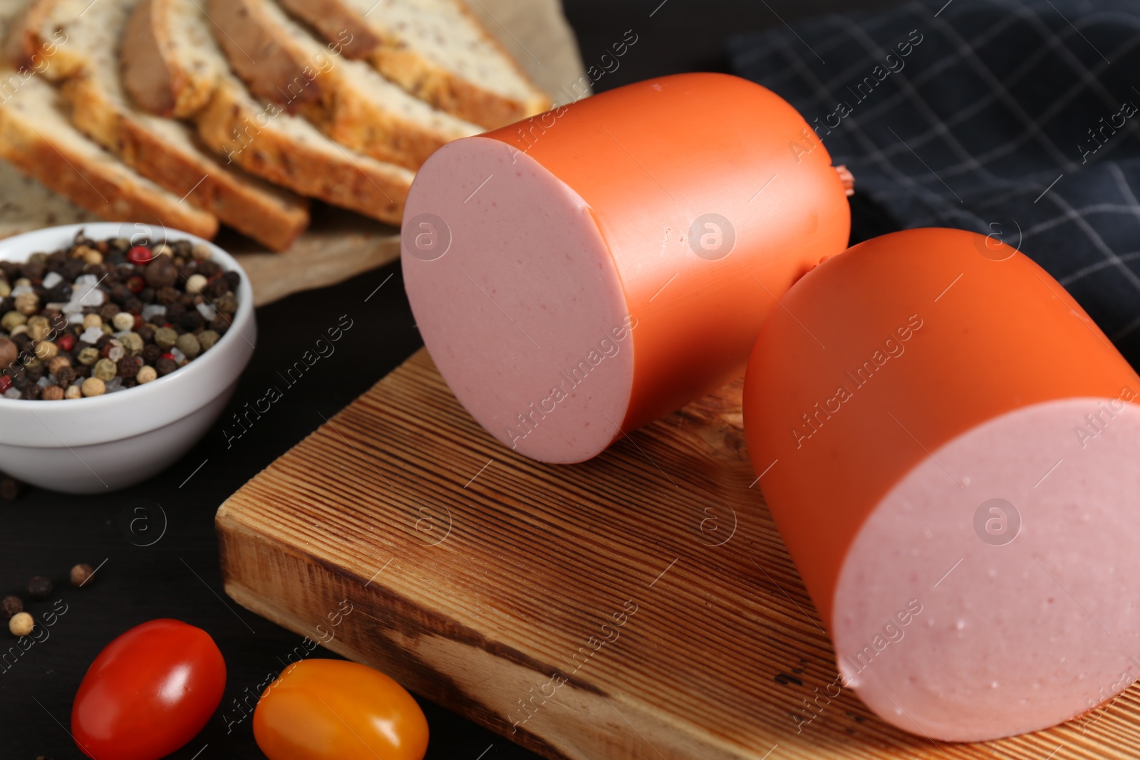 Photo of Tasty boiled sausage, tomatoes, spices and bread on black table, closeup