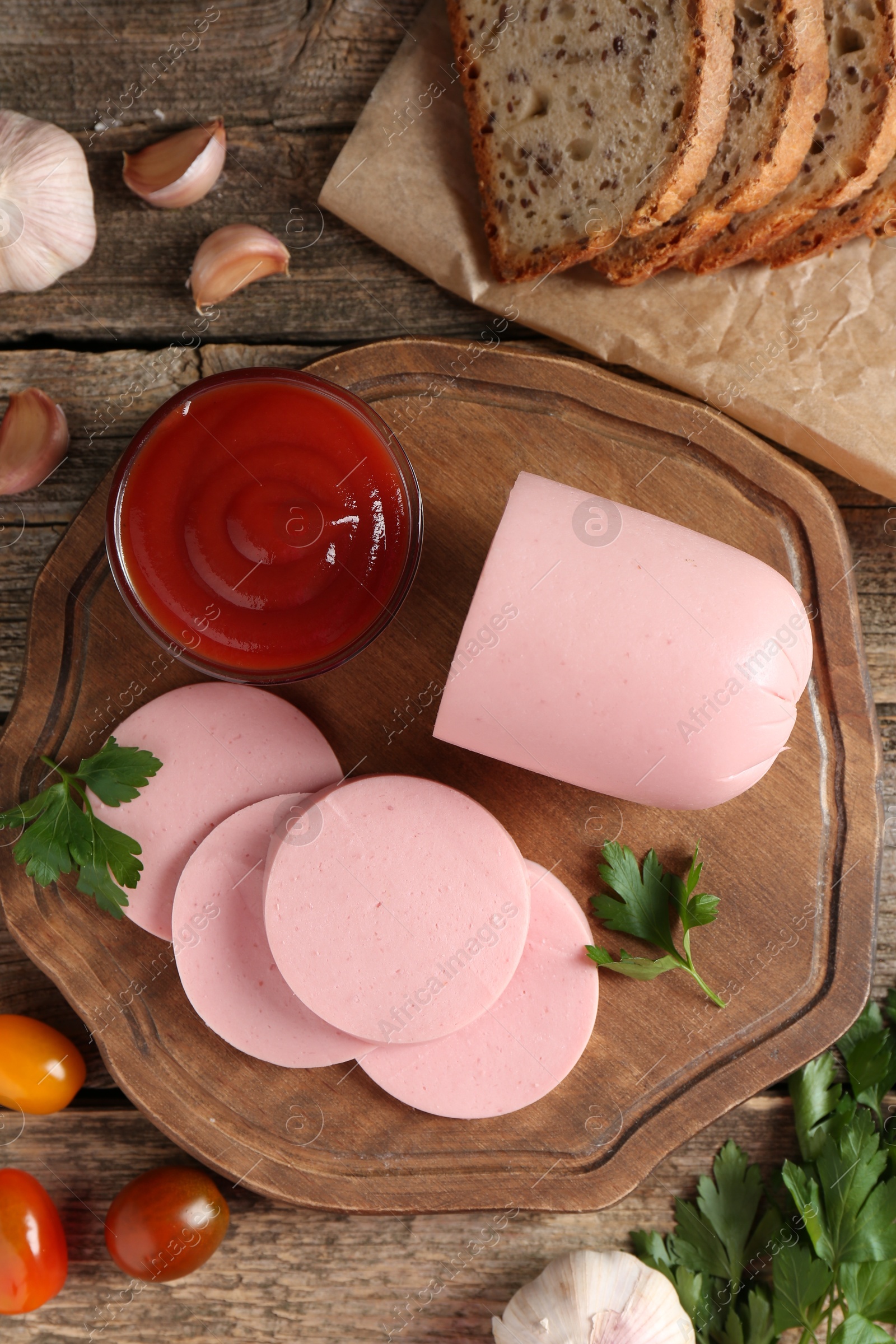 Photo of Tasty boiled sausage, ketchup, tomatoes, spices and bread on wooden table, top view